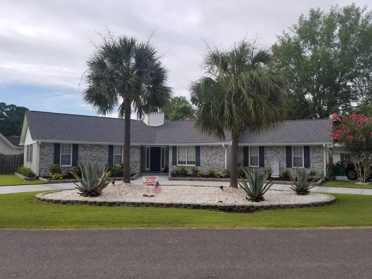 This exterior shot features the front yard of the property, complete with palm trees, a well-maintained landscaped lawn, and a 'Yard of the Month' sign. The inviting atmosphere suggests plenty of space for kids to play and for families to host outdoor activities and barbecues under the sun.