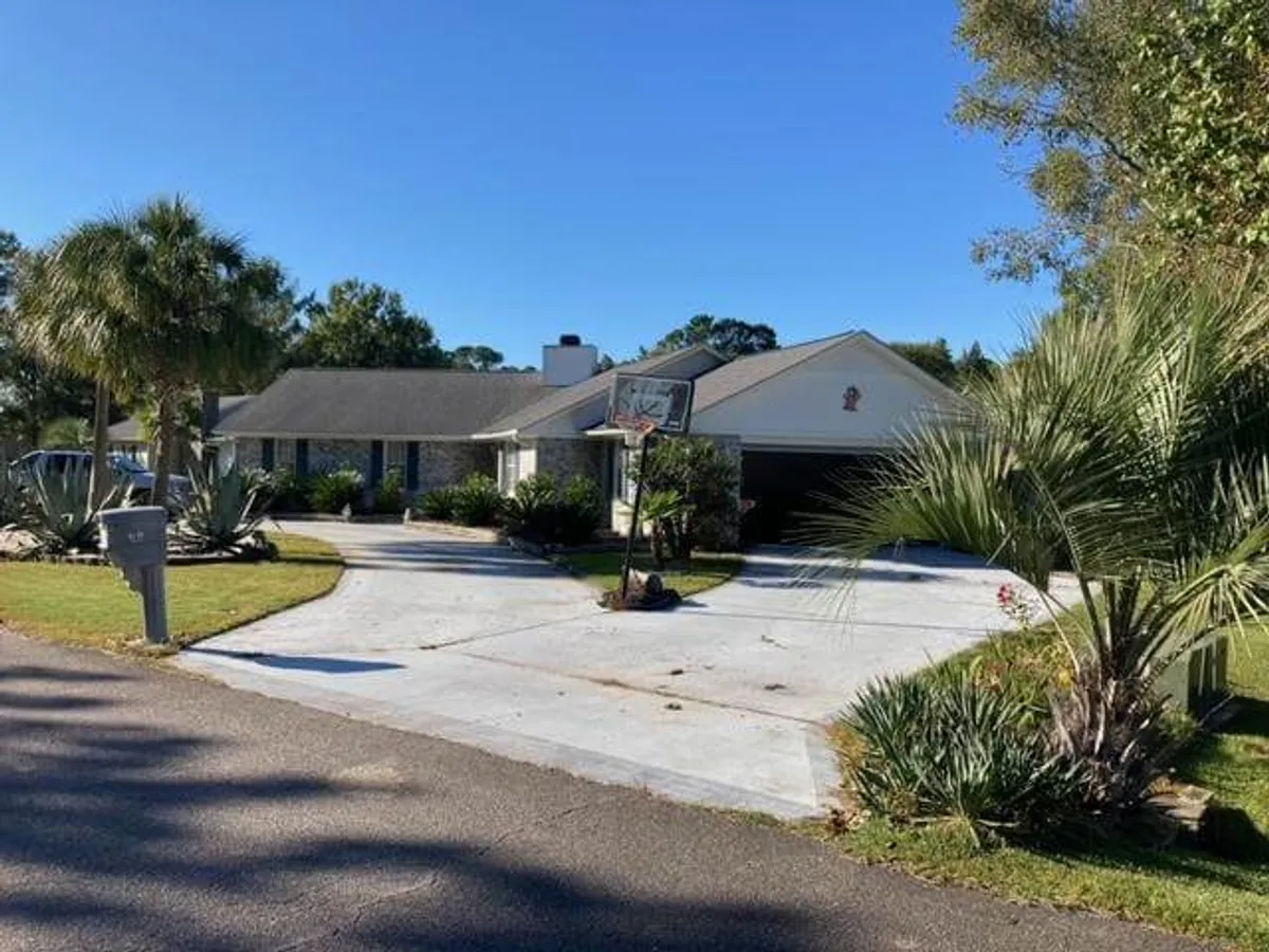 This image features the front driveway leading up to the house, with a basketball hoop and well-kept landscaping. The driveway is spacious, and the view hints at the home's garage area, connecting strongly to the arrival and storage theme.