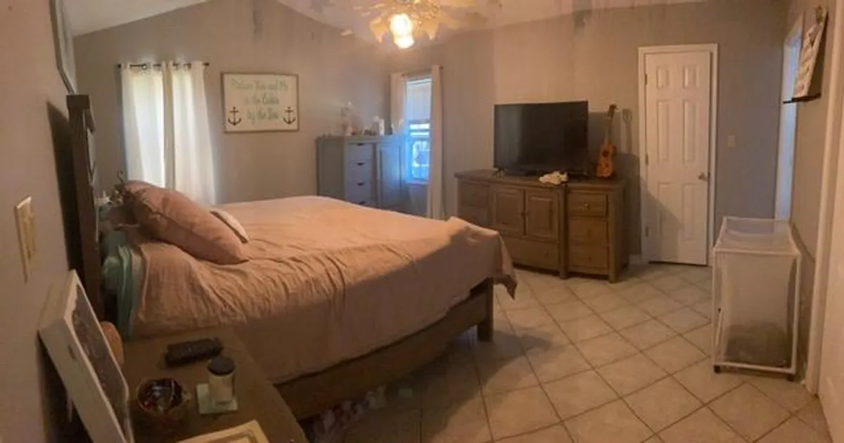 A serene bedroom scene featuring a king-size bed, a soft glow of natural light filtering in through the window, and a flatscreen television atop a cozy dresser. The space exudes tranquility, inviting guests to relax, read, or enjoy a quiet movie night together in comfort.