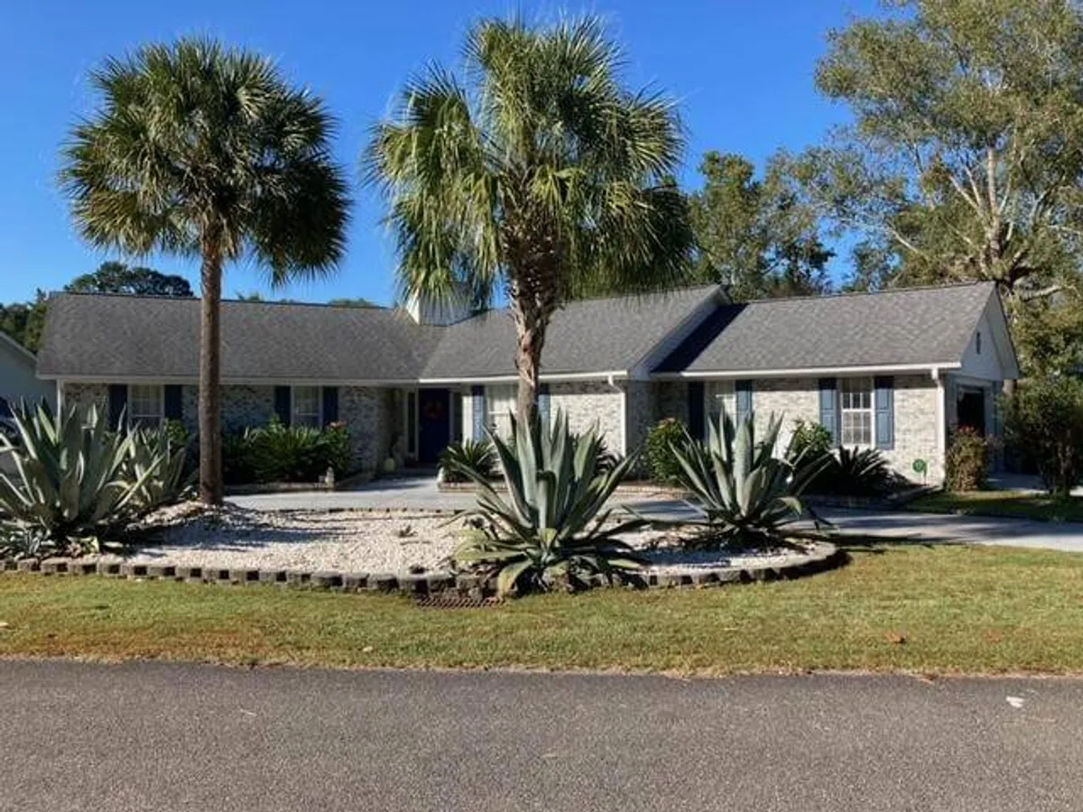 The exterior of the home with a stone facade, lush palm trees, and a neatly landscaped garden. The scene suggests a welcoming atmosphere, with ample space for guests to relax, enjoy morning coffee, or participate in outdoor gatherings.