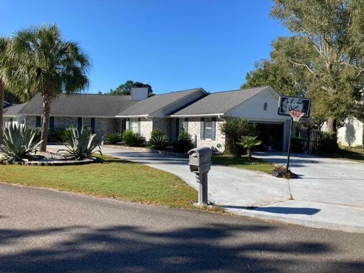 The image presents a broader exterior view of the property, showing a single-story house set amidst palm trees, a landscaped yard, and a basketball hoop. The area is suitable for family sports and casual outdoor games, adding another layer of fun to the stay.