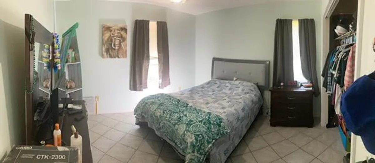 This image showcases a comfortable bedroom with a bed dressed in patterned bedding, a dresser, stylish lion artwork on the wall, and a clothing rack. The room is softly lit, evoking a sense of relaxation and personal space.