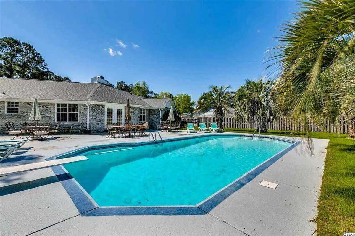 The image showcases a sparkling private inground pool surrounded by comfortable patio furniture and lush landscape greenery. The setting basks in the warm glow of a sunset, inviting guests to relax, dine outdoors, or enjoy a morning coffee by the water's edge. The fenced-in yard emphasizes privacy and tranquility.
