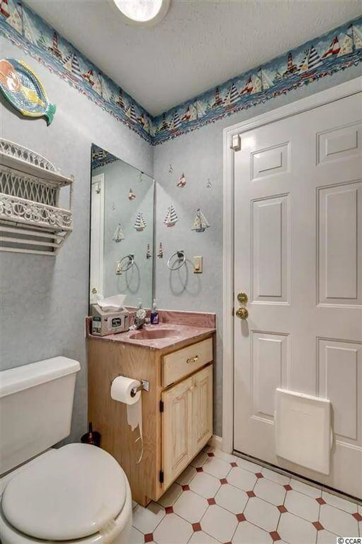 A playful interior bathroom scene with sailboat wallpaper, a pink countertop, and a wooden cabinet with a mirror. The whimsical décor suggests a dedicated, easily accessible space for pool users to rinse off or change, fitting the description of a 'pool bathroom.'